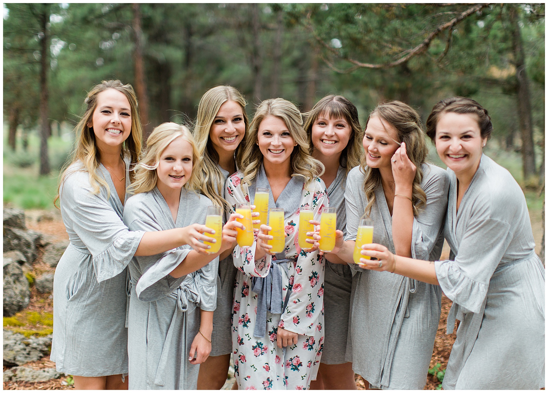 McKenna and her bridesmaids standing together in their robes in the midst of getting ready for the day with their mimosas smiling.