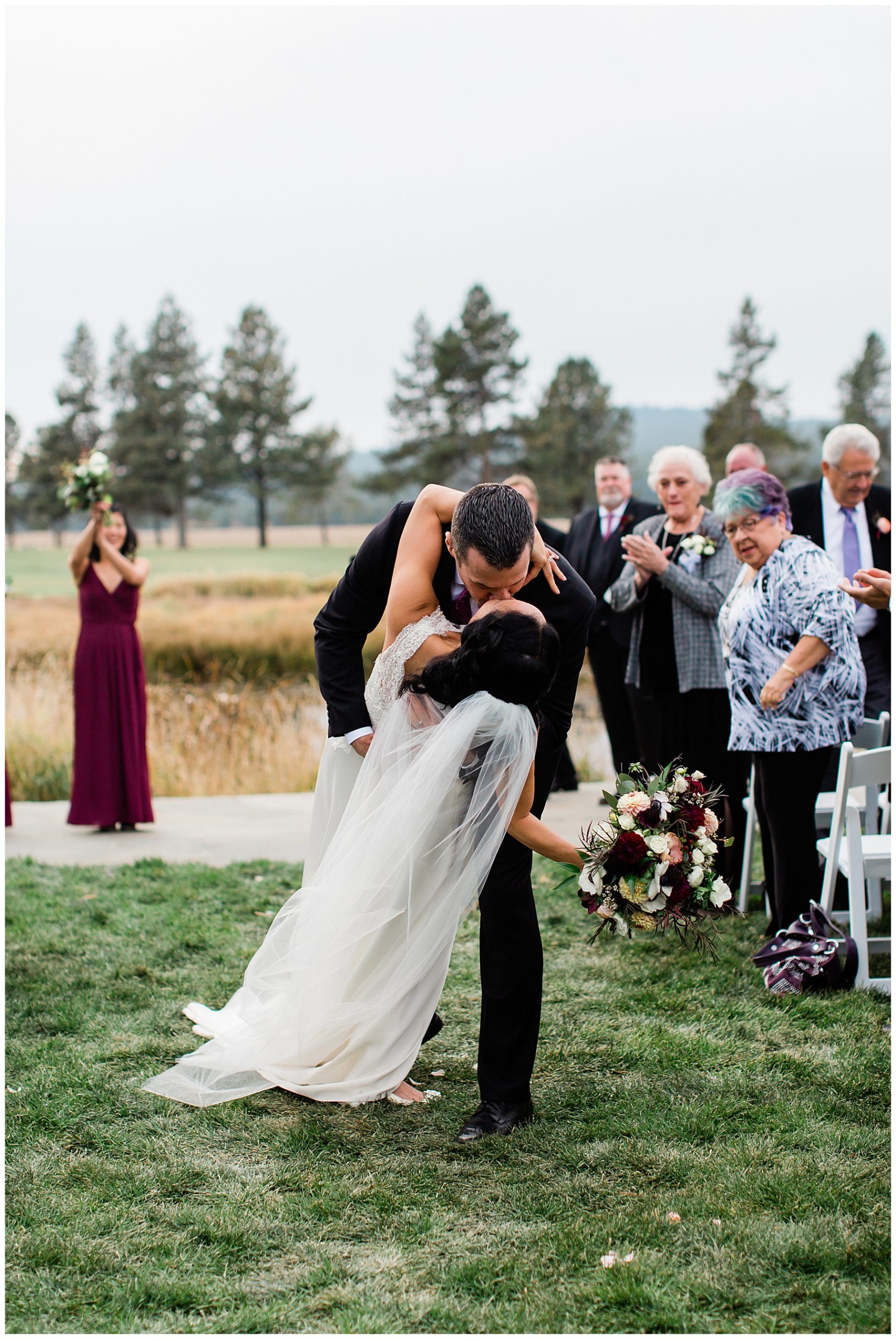 A portrait of the newlyweds having a kiss in the middle of their walk down the aisle at the Sunriver Resort Fall Riverfront Wedding