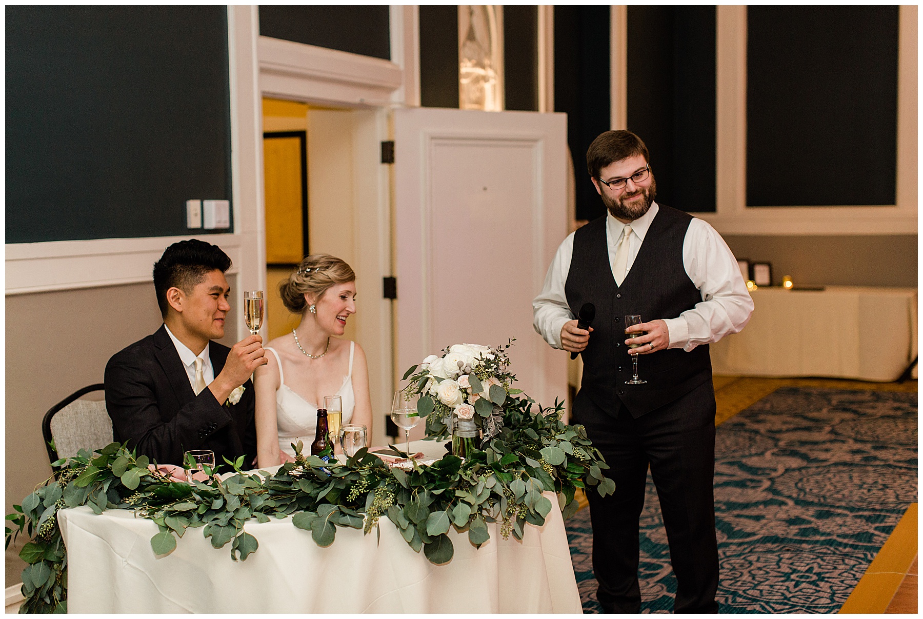 best man gives a toast in the sentinel hotel ballroom. the sweetheart table is covered in lush greenery