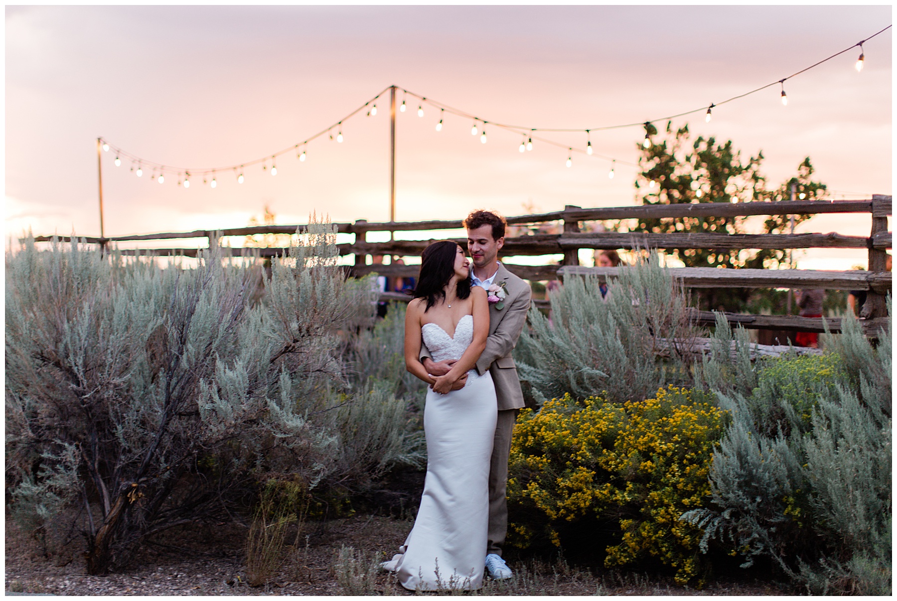 The happily married couple taking a portrait against the bushes with the warm sun setting in the distance. 